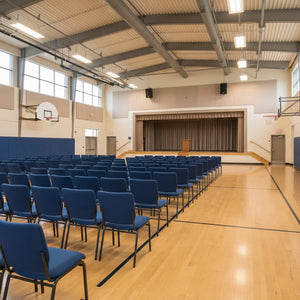 Large indoor gymnasium with blue chairs arranged in rows and a stage at the back.